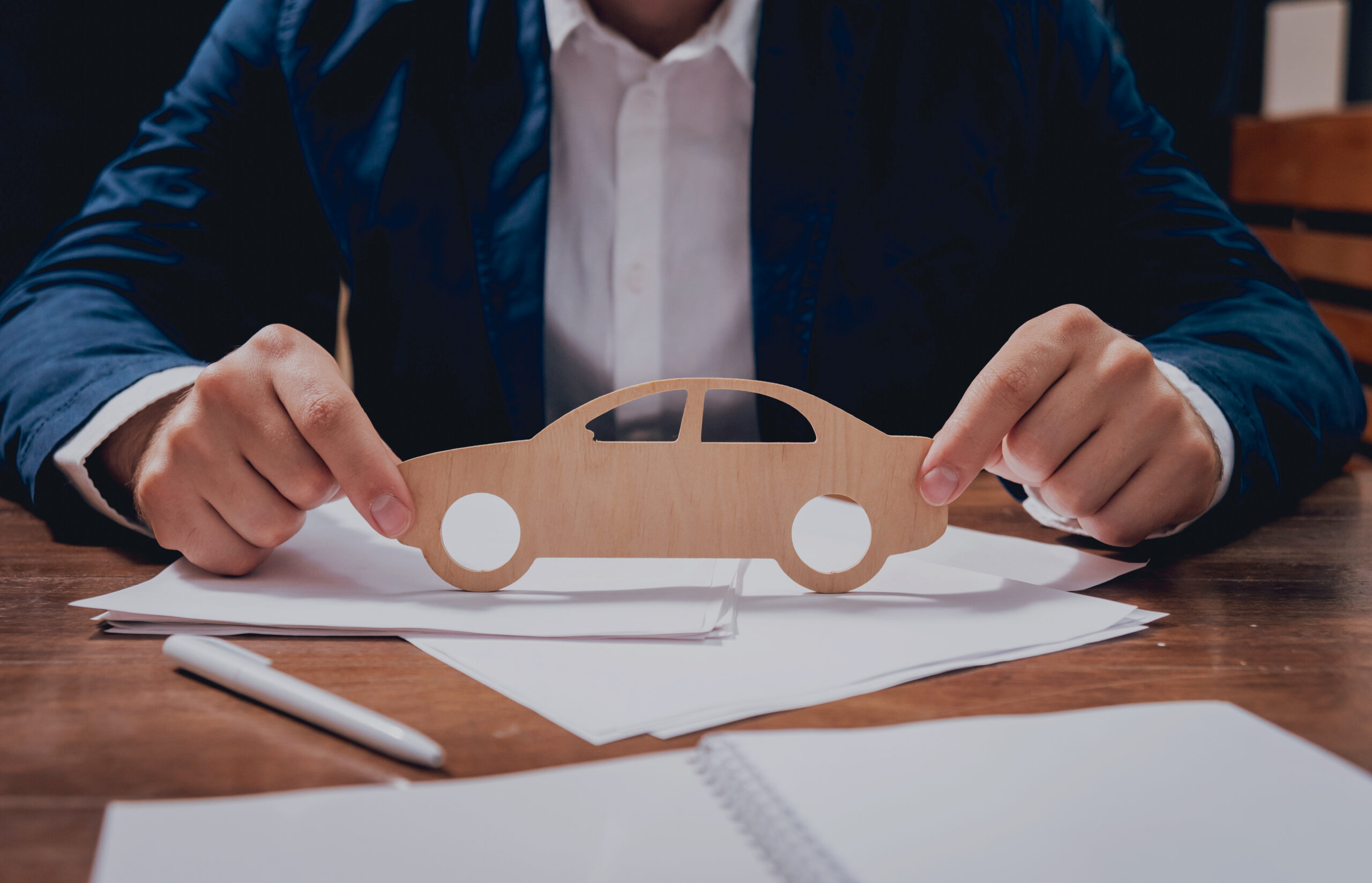Man proposing signing a car insurance policy, the agent is holding the wooden car model. Car insurance concept.