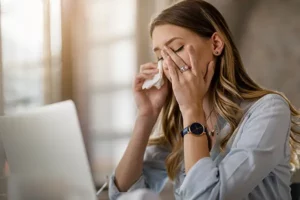 Personas en una oficina experimentando síntomas como dolores de cabeza, fatiga e irritación ocular debido al Síndrome del Edificio Enfermo.